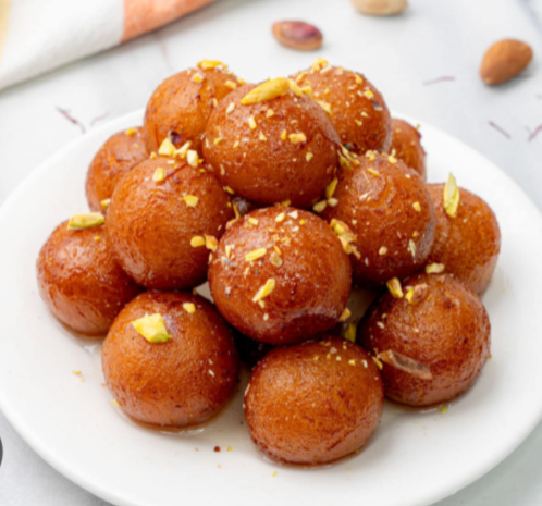 A plate of soft and juicy Golap Jamun soaked in sugar syrup, garnished with chopped pistachios.