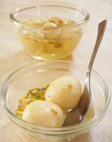 Soft and spongy Bengali Rasgulla soaked in sugar syrup, served in a bowl.