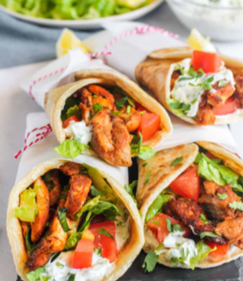 Homemade Chicken Shawarma wrap with grilled chicken, fresh vegetables, and garlic sauce on a wooden platter.