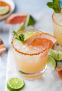 A refreshing Paloma cocktail served in a highball glass with ice, garnished with a grapefruit wedge and a salted rim.