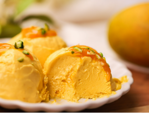 Scoops of homemade mango ice cream in a bowl, topped with fresh mango chunks and nuts