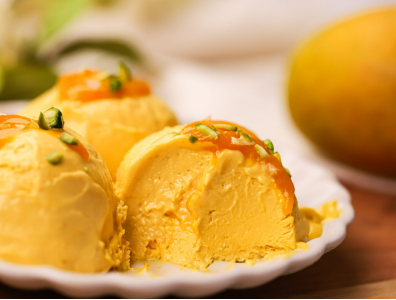 Scoops of homemade mango ice cream in a bowl, topped with fresh mango chunks and nuts